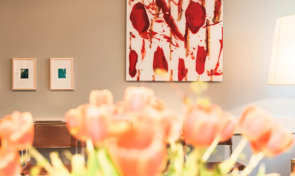 Blick über einen Tulpenstrauß auf eine Wand mit einem großen und zwei kleinen Bildern.